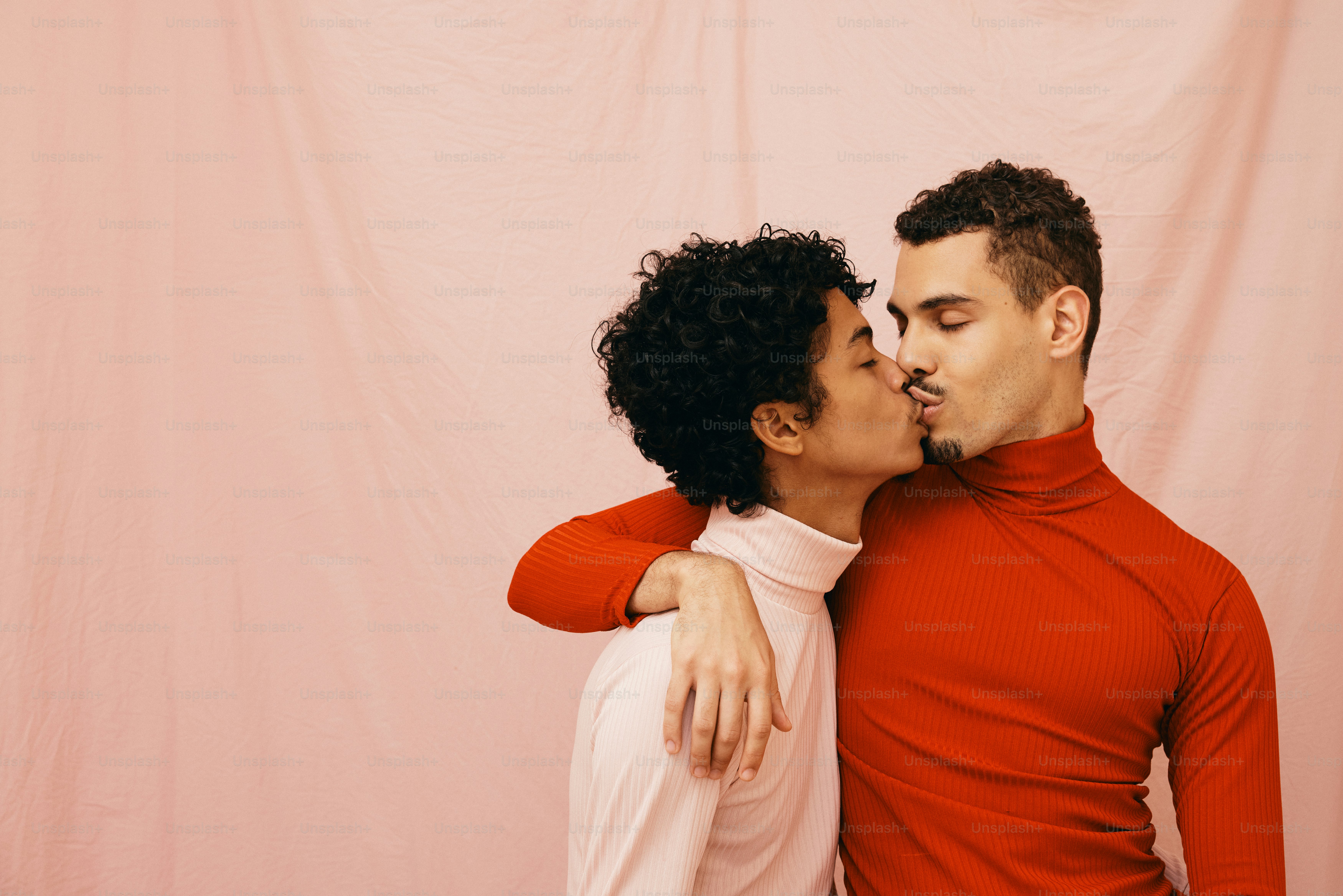 a man and woman kissing each other in front of a pink backdrop